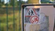 Sticker na słupie z napisem „Stop pedofilom” w przestrzeni publicznej – wyraz społecznego sprzeciwu wobec przemocy seksualnej wobec dzieci, zdjęcie wykonane w naturalnym świetle przy ogrodzeniu, Polska.