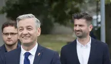 Robert Biedroń i Krzysztof Śmiszek podczas wydarzenia politycznego – liderzy Nowej Lewicy w formalnych garniturach, uśmiechnięci na tle zieleni.
