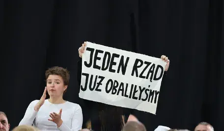 remier Donald Tusk podczas spotkania z mieszkańcami Piotrkowa Trybunalskiego. W tle protestujący z transparentami i zwolennicy skandujący jego imię.