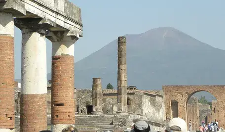 Ruiny starożytnego miasta Pompeje we Włoszech – widok na zachowane fragmenty budowli, brukowaną ulicę i pozostałości amfiteatru na tle Wezuwiusza.