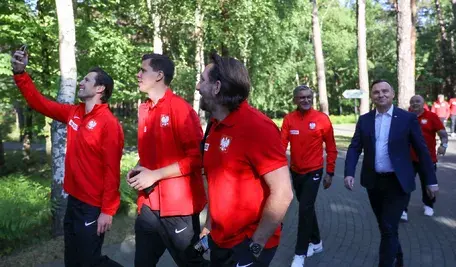 Grzegorz Krychowiak w towarzystwie Wojciecha Szczęsnego i Tomasza Iwana na spotkaniu z prezydentem Andrzejem Dudą. Piłkarze reprezentacji Polski spacerują w towarzystwie prezydenta RP w ośrodku treningowym. Zawodnicy w czerwonych dresach kadry narodowej robią wspólne zdjęcie podczas luźnej rozmowy w lesie.
