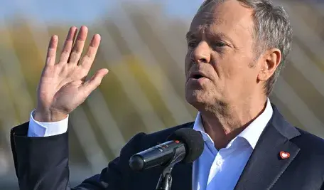 Donald Tusk pokazuje 5 palców i robi usta w dziubek. Na klapie ma puste serduszko, logo KO i zapewnia, że poprze PSL w zniesieniu dwukadencyjności w samorządachg