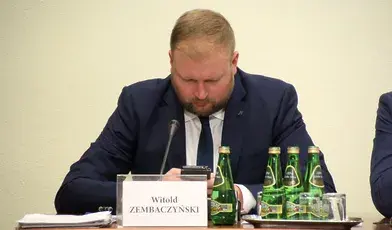 Poseł Witold Zembaczyński podczas wystąpienia na komisji, patrzy w telefon, w garniturze i krawacie, z mikrofonem przed sobą – ilustracja do artykułu o kontrowersyjnej wypowiedzi polityka