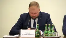Poseł Witold Zembaczyński podczas wystąpienia na komisji, patrzy w telefon, w garniturze i krawacie, z mikrofonem przed sobą – ilustracja do artykułu o kontrowersyjnej wypowiedzi polityka