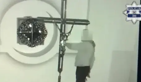 Nagranie z monitoringu pokazujące zamaskowanego włamywacza wewnątrz kościoła w Żorach, stojącego przy dużym krzyżu podczas aktu dewastacji.