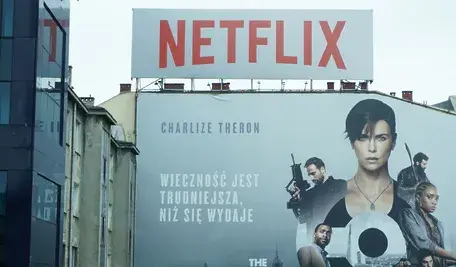 alt: Billboard Netflixa z plakatem filmu z Charlize Theron na fasadzie budynku – reklama platformy streamingowej w przestrzeni miejskiej przedstawiona w kontekście łączenia Netflixa z HBO
