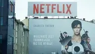 alt: Billboard Netflixa z plakatem filmu z Charlize Theron na fasadzie budynku – reklama platformy streamingowej w przestrzeni miejskiej przedstawiona w kontekście łączenia Netflixa z HBO