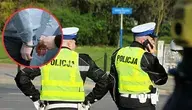 Dwóch policjantów w kamizelkach odblaskowych z napisem 'Policja' stoi na ulicy, jeden rozmawia przez telefon. W lewym górnym rogu zdjęcia znajduje się wstawka przedstawiająca osobę w kajdankach.