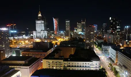 Panorama Warszawy nocą z podświetlonymi wieżowcami i charakterystyczną architekturą śródmieścia, widok na centrum stolicy Polski oświetlone światłami miasta