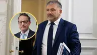 Waldemar Żurek w garniturze trzyma dokumenty i wychodzi z pokoju, obok widoczny Marcin Romanowski w okrągłej ramce.