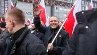 Uczestnicy marszu z biało-czerwonymi flagami w centrum Warszawy, prezydent Karol Nawrocki na pierwszym planie uśmiecha się i macha do tłumu.