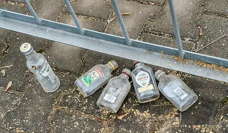 Porzucone małe butelki po alkoholu („małpki”) leżące na chodniku przy metalowym ogrodzeniu..