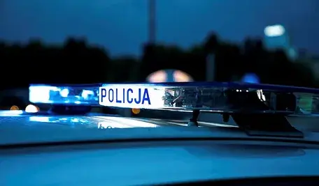 Radiowóz policji z włączonymi niebieskimi sygnałami świetlnymi po zmroku.
