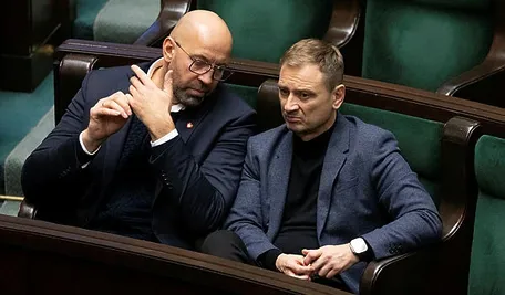 „Jakub Rutnicki i Sławomir Nitras siedzą w ławach parlamentu, rozmawiają ze sobą podczas obrad.