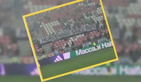 Transparent kibiców Maccabi Hajfa z napisem „Mordercy od 1939 roku”, wywieszony na trybunach podczas meczu z Rakowem Częstochowa; tłum izraelskich fanów stoi za bannerm, trzymając go nad barierką stadionu