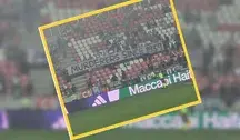 Transparent kibiców Maccabi Hajfa z napisem „Mordercy od 1939 roku”, wywieszony na trybunach podczas meczu z Rakowem Częstochowa; tłum izraelskich fanów stoi za bannerm, trzymając go nad barierką stadionu