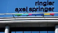 Logo firmy Ringier Axel Springer umieszczone na dachu nowoczesnego budynku, na tle jasnego, bezchmurnego nieba.