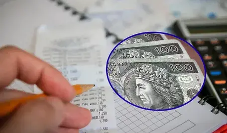 „Osoba liczy domowe wydatki na podstawie paragonu, obok leży kalkulator i notes w kratkę. Nałożone koło pokazuje banknoty 100 zł, symbolizując rosnące koszty i obciążenia finansowe.