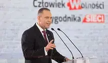 Prezydent Karol Nawrocki przemawia przy podium z dwoma mikrofonami podczas uroczystego wydarzenia. W tle widoczny jest baner z napisem ‘Człowiek Wolności Tygodnika Sieci’