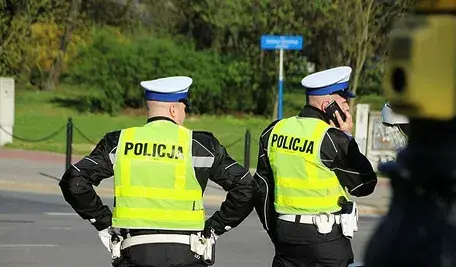 Dwaj policjanci w mundurach stoją na ulicy, jeden z nich rozmawia przez telefon.