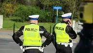 Dwaj policjanci w mundurach stoją na ulicy, jeden z nich rozmawia przez telefon.