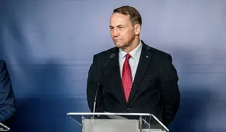 Radosław Sikorski stojący przy mównicy podczas oficjalnej konferencji prasowej.