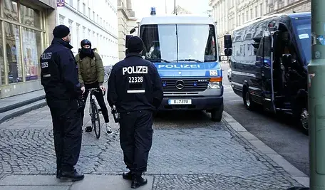 Radiowóz niemieckiej policji zaparkowany na ulicy, obok dwóch policjantów w mundurach.