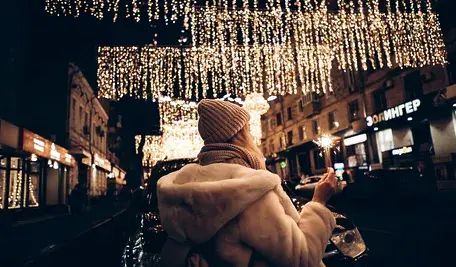 Niemiecki jarmark świąteczny z oświetlonymi stoiskami i tłumem odwiedzających na tle dekoracji bożonarodzeniowych.”