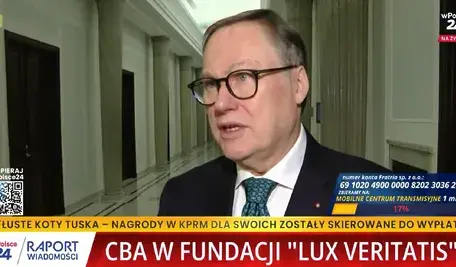 Senator PiS Grzegorz Bierecki udziela wypowiedzi przed kamerą w jasnym korytarzu sejmowym. Na ekranie widać paski informacyjne stacji wPolsce24 dotyczące działań CBA w Fundacji ‘Lux Veritatis’ oraz komentarze polityczne w sprawie przeszukania związanego z postępowaniem dotyczącym Funduszu Sprawiedliwości.