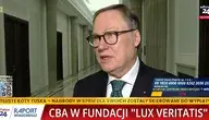 Senator PiS Grzegorz Bierecki udziela wypowiedzi przed kamerą w jasnym korytarzu sejmowym. Na ekranie widać paski informacyjne stacji wPolsce24 dotyczące działań CBA w Fundacji ‘Lux Veritatis’ oraz komentarze polityczne w sprawie przeszukania związanego z postępowaniem dotyczącym Funduszu Sprawiedliwości.