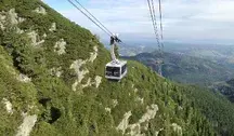 Kolejka linowa nad górskimi stokami w Tatrach, wagonik poruszający się nad zalesionym zboczem i rozległą panoramą Podhala w tle.