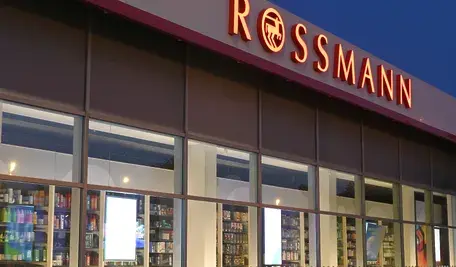 Wejście do drogerii Rossmann z charakterystycznym czerwonym logo na elewacji.