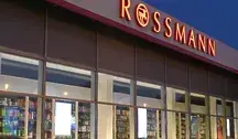 Wejście do drogerii Rossmann z charakterystycznym czerwonym logo na elewacji.