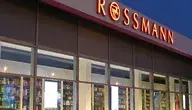 Wejście do drogerii Rossmann z charakterystycznym czerwonym logo na elewacji.