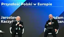 Jarosław Kaczyński i Adam Bielan siedzą na scenie podczas publicznej dyskusji. Obaj trzymają mikrofony i uśmiechają się, a za nimi widoczna jest duża plansza z napisem dotyczącym przyszłości Polski w Europie.