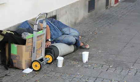 Osoba leżąca na ulicy z bagażami.