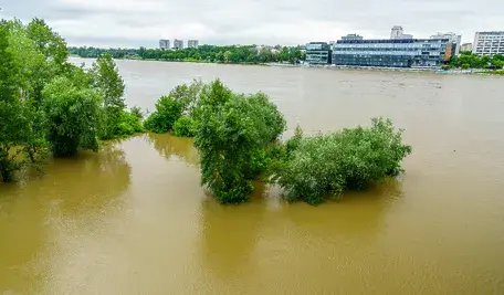Zalany teren po ostatniej powodzi - woda sięga fundamentów domów, w tle widać uszkodzone drogi i błotniste podwórza