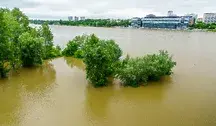 Zalany teren po ostatniej powodzi - woda sięga fundamentów domów, w tle widać uszkodzone drogi i błotniste podwórza
