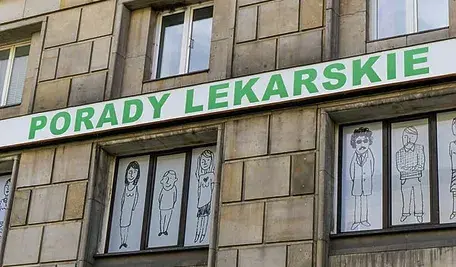 Budynek z szyldem „Porady lekarskie” na tle okien ozdobionych rysunkami postaci.