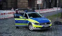 Niemiecki radiowóz policyjny stoi na ulicy, a obok niego znajduje się funkcjonariusz policji w umundurowaniu.