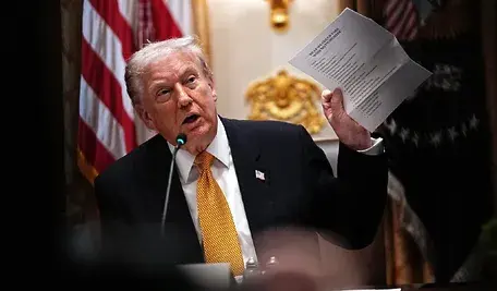 Donald Trump przemawia podczas konferencji w Białym Domu, trzymając dokument w ręku.