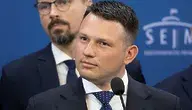 Sławomir Mentzen w garniturze i krawacie stoi przy mównicy na tle niebieskiej ścianki z logo Sejmu; za nim widoczny jest drugi mężczyzna w okularach.