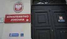 Wejście do budynku Ministerstwa Zdrowia z czerwonym szyldem i godłem Polski nad drzwiami.