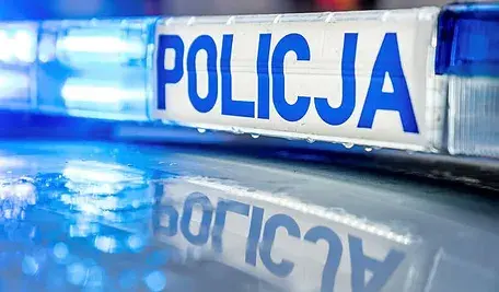 Niebiesko-białe światła policyjnego radiowozu z wyraźnym napisem ‘Policja’ widocznym na belce świetlnej.