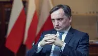 Zbigniew Ziobro siedzący w biurze z dłońmi złożonymi przed sobą; w tle widać polskie flagi.
