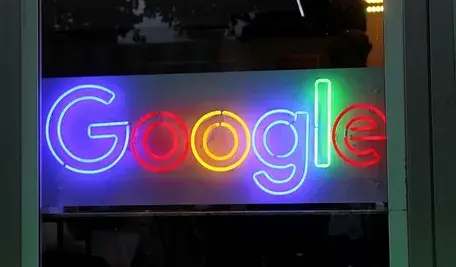 Neonowe logo Google świecące w kolorach niebieskim, czerwonym, żółtym i zielonym na tle przeszklonej witryny.