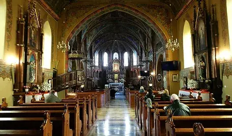Wnętrze zabytkowego kościoła katolickiego podczas Mszy Świętej – wierni siedzą w drewnianych ławkach, w tle ołtarz i bogato zdobione sklepienie.