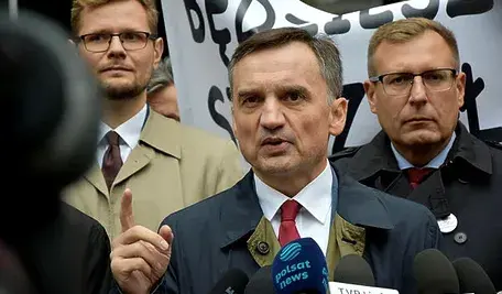 Zbigniew Ziobro podczas wystąpienia, przemawiający na tle transparentu w otoczeniu innych polityków.