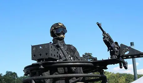 Żołnierz Sił Zbrojnych RP w umundurowaniu bojowym, uzbrojony w karabin maszynowy, podczas ćwiczeń wojskowych na otwartym terenie.