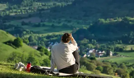 Kobieta odpoczywająca na wzgórzu z widokiem na zieloną dolinę i górską miejscowość, relaks na łonie natury